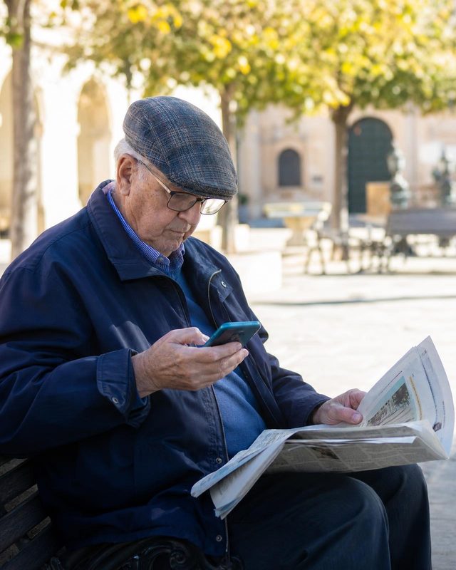 Un hombre mayor consulta el móvil con el periódico en el regazo